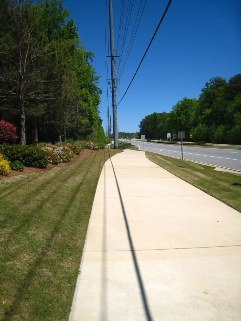 A sidewalk with grass and bushes on the side of it.