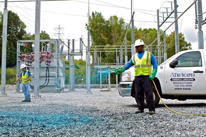 A man in yellow vest holding hose near white car.