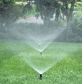 A field with three sprinklers spraying water.