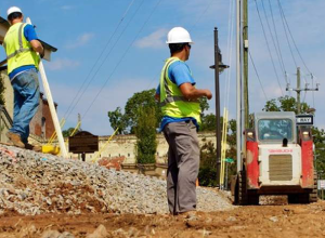 A man in yellow vest standing on dirt road.