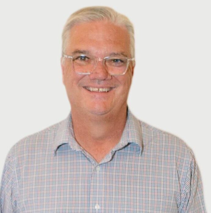 A man with white hair and glasses is smiling.